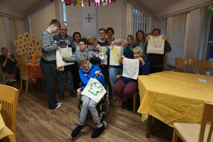 Eine Gruppe von Menschen sitzt in einem Raum. Manche halten Papierbilder hoch.