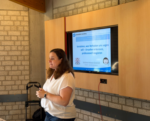 Eine Frau steht vor einer Backsteinwand und spricht. Sie hält ein Mikrofon in der Hand.