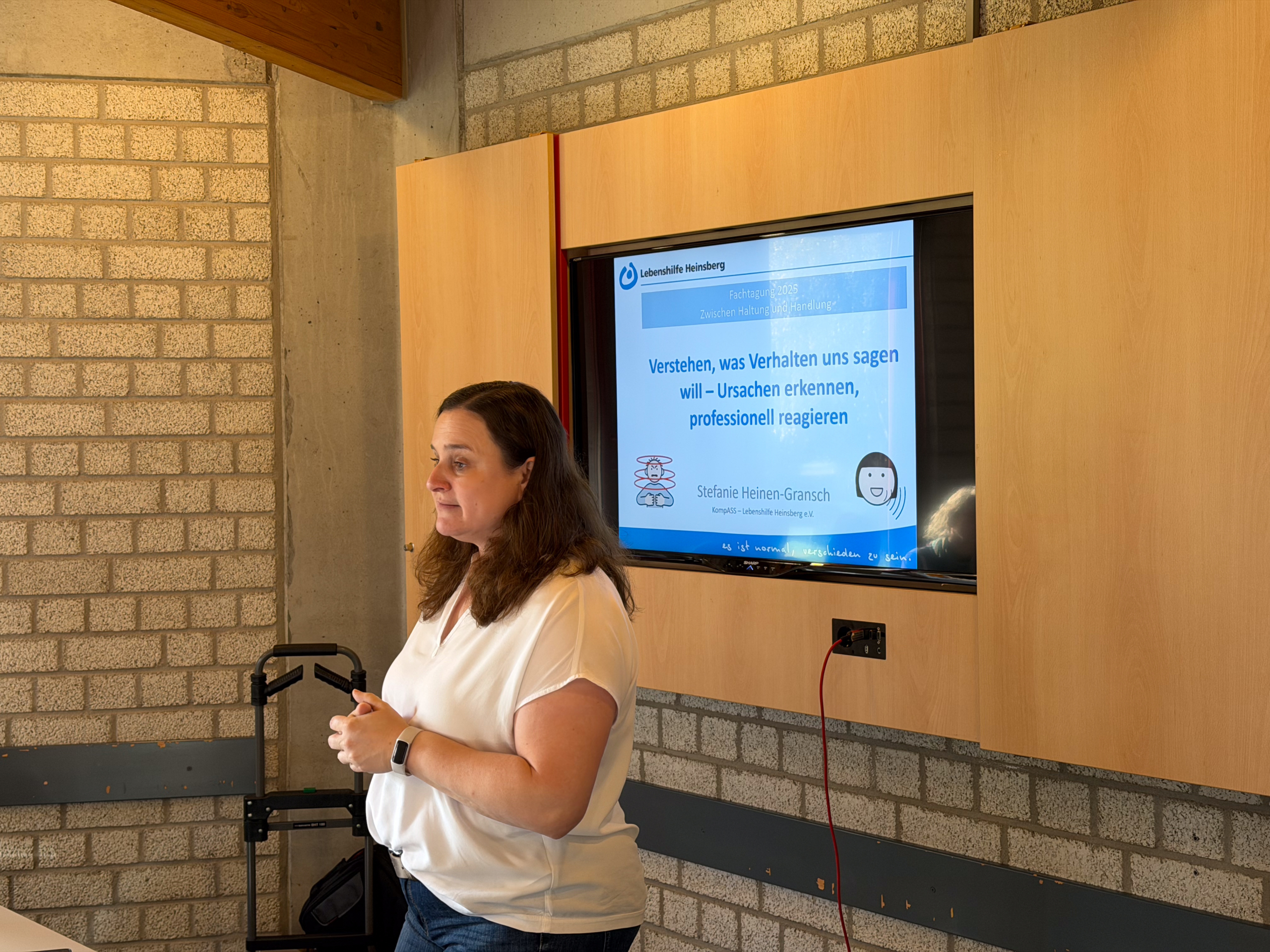 Eine Frau steht vor einer Backsteinwand und spricht. Sie hält ein Mikrofon in der Hand.
