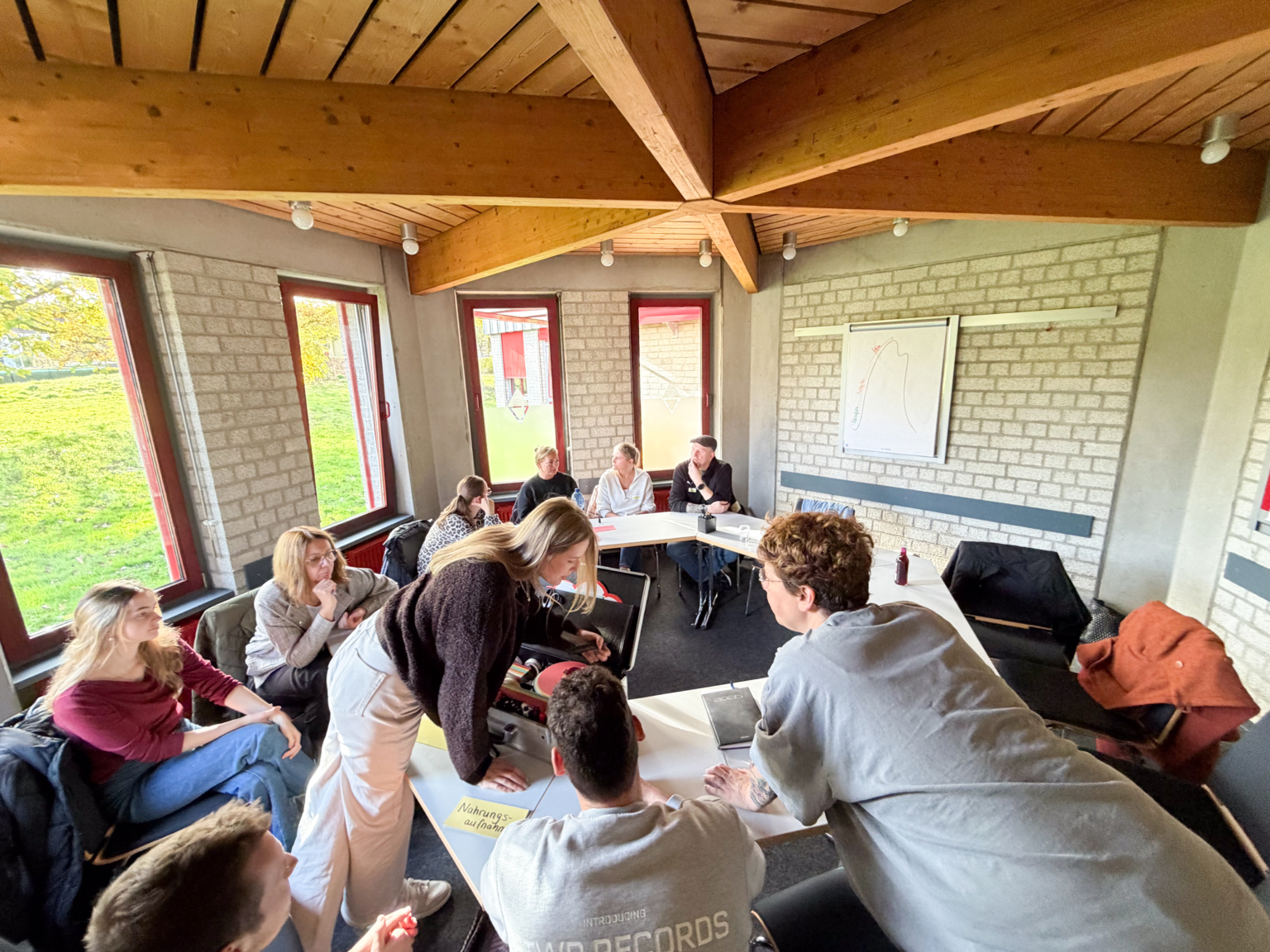 Menschen sitzen in einem Raum zusammen. Sie unterhalten sich und schauen auf etwas.