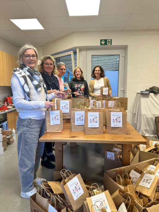 Frauen packen Geschenke in braune Tüten. Sie stehen an einem Tisch mit vielen Tüten.