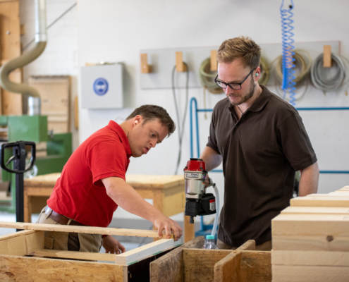 Zwei Männer arbeiten mit einem Werkzeug an Holz.