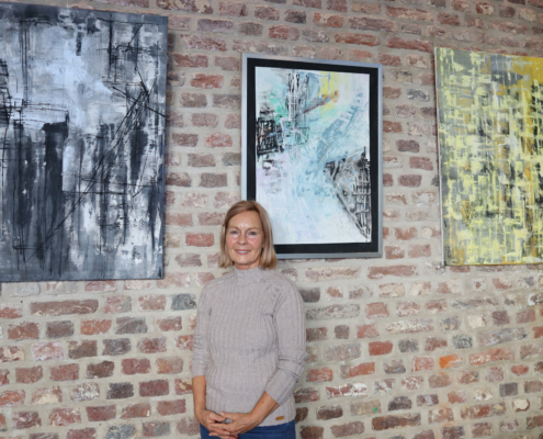 Frau steht vor drei Bildern. Zwei sind schwarz-weiß, eines ist blau. Die Bilder hängen an einer Mauer.