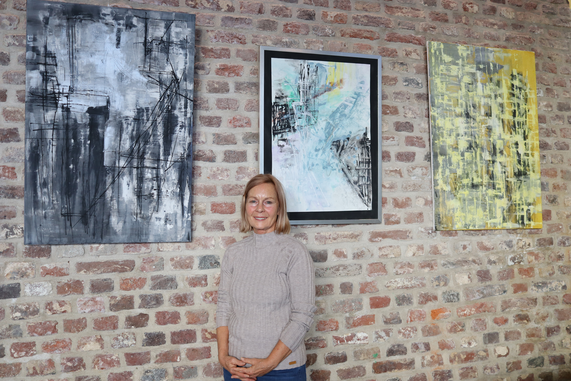 Frau steht vor drei Bildern. Zwei sind schwarz-weiß, eines ist blau. Die Bilder hängen an einer Mauer.