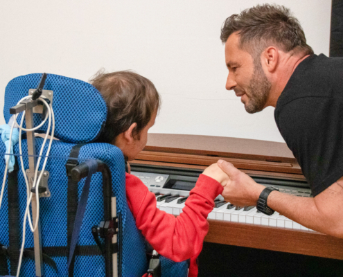 Ein Mann hilft einem Kind am Klavier zu sitzen. Das Kind spielt Klavier.
