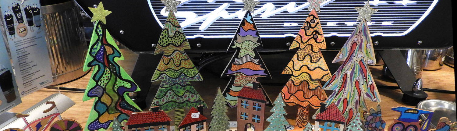 Bunte Pappfiguren von Weihnachtsbäumen und Häusern stehen auf einem Tisch. Es sieht nach einer lustigen Weihnachtsdeko aus.