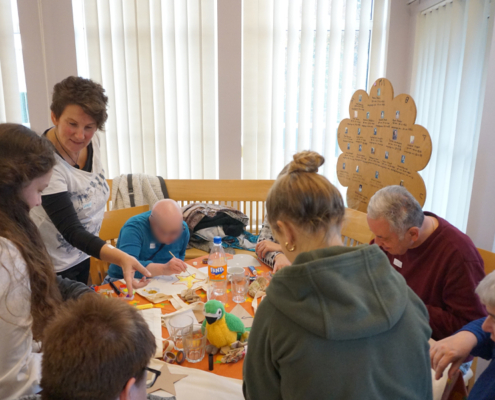 Menschen sitzen an einem Tisch. Sie schauen sich etwas an. Es sind viele Sachen auf dem Tisch.