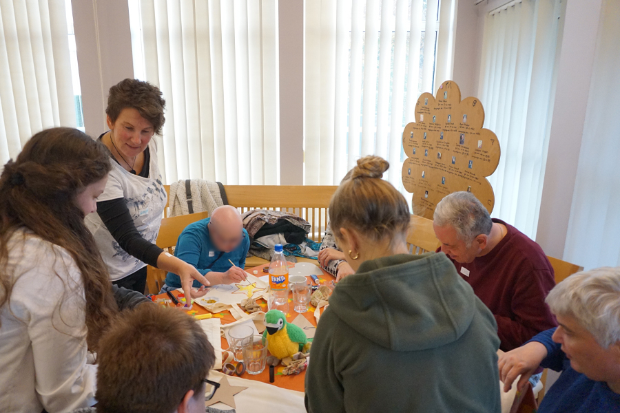 Menschen sitzen an einem Tisch. Sie schauen sich etwas an. Es sind viele Sachen auf dem Tisch.