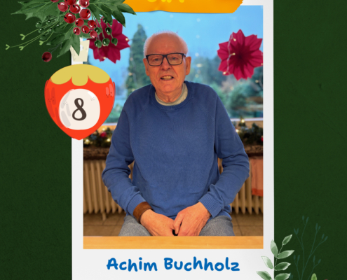 Ein älterer Mann mit Brille steht vor einem Garten. Er trägt einen blauen Pullover.