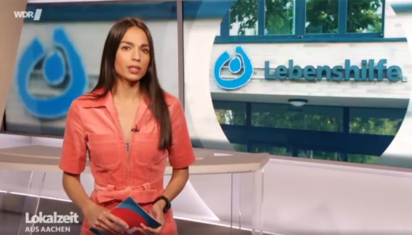 Eine Frau steht vor einem roten Hintergrund. Sie trägt ein rotes Oberteil und eine Uhr am Handgelenk.