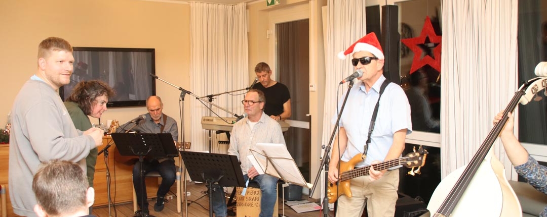 Eine Band spielt auf einer Bühne. Es sind fünf Männer zu sehen. Einer spielt Klavier, einer trägt einen Weihnachtsmannhut und spielt Bass.