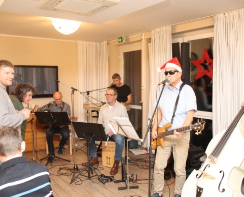 Eine Band spielt auf einer Bühne. Es sind fünf Männer zu sehen. Einer spielt Klavier, einer trägt einen Weihnachtsmannhut und spielt Bass.
