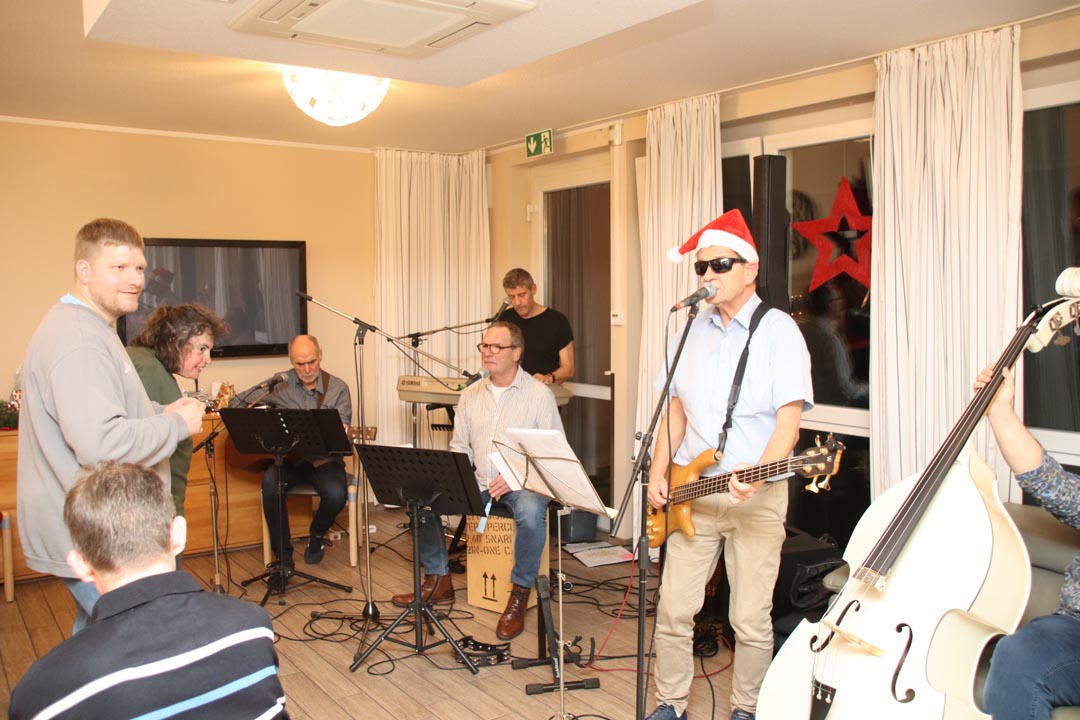 Eine Band spielt auf einer Bühne. Es sind fünf Männer zu sehen. Einer spielt Klavier, einer trägt einen Weihnachtsmannhut und spielt Bass.