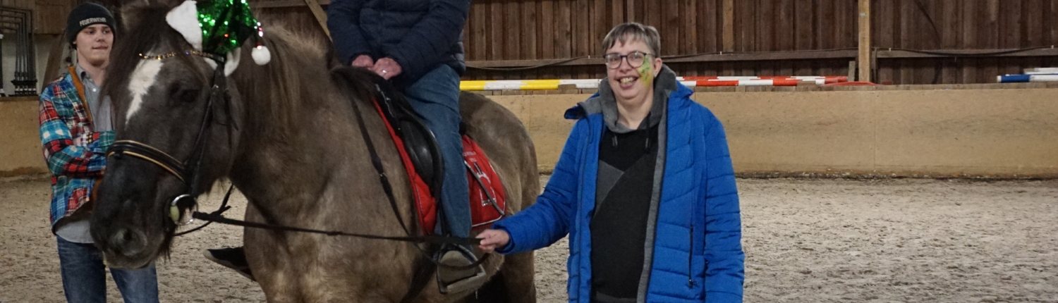 Ein Mann sitzt auf einem Pferd. Zwei Frauen stehen daneben. Sie sind in einem Stall.