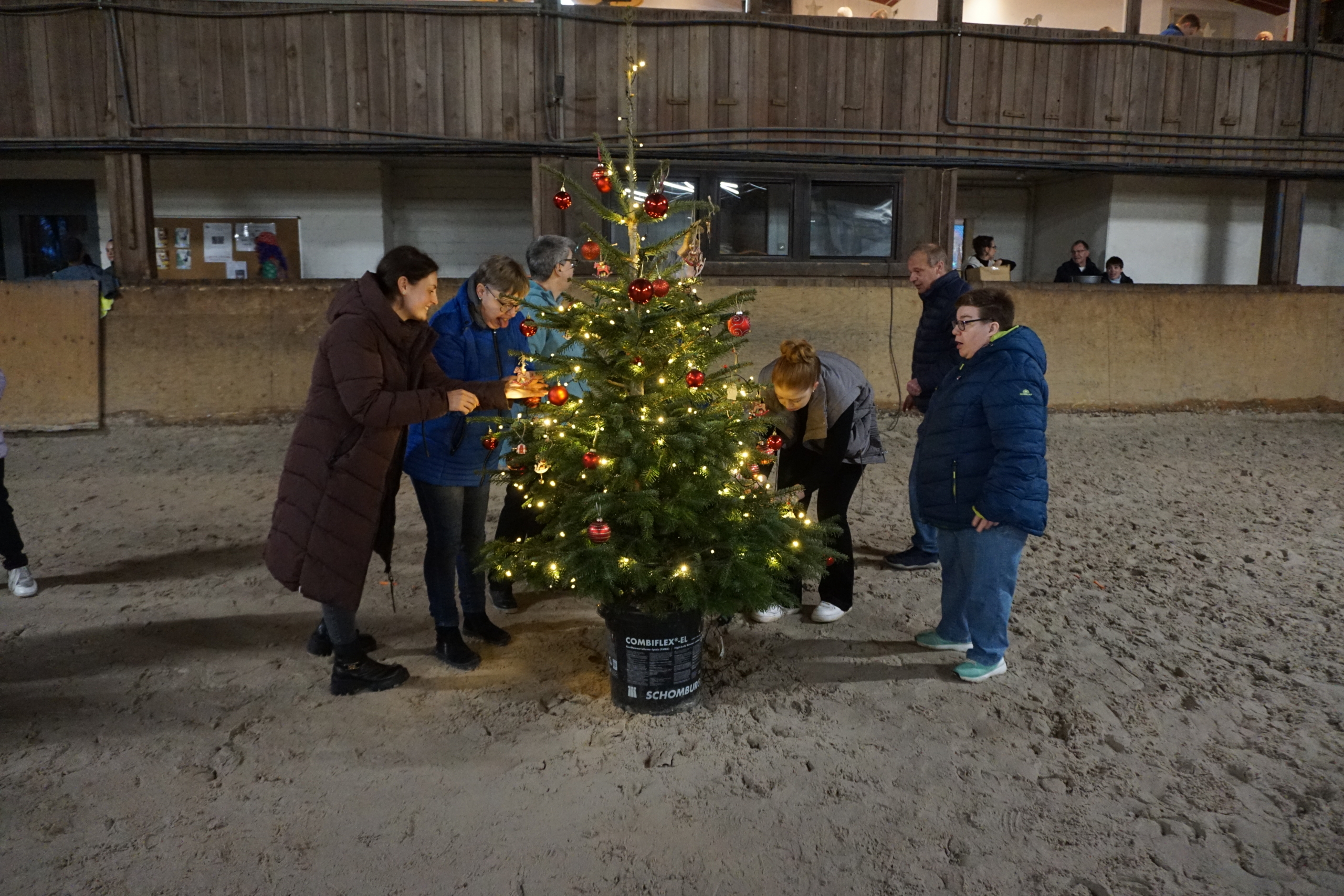 Menschen stellen einen Weihnachtsbaum auf. Es ist dunkel draußen.