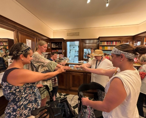 Leute stehen an einem Tresen. Eine Person gibt etwas in eine Hand. Hinter dem Tresen ist ein Mann zu sehen.