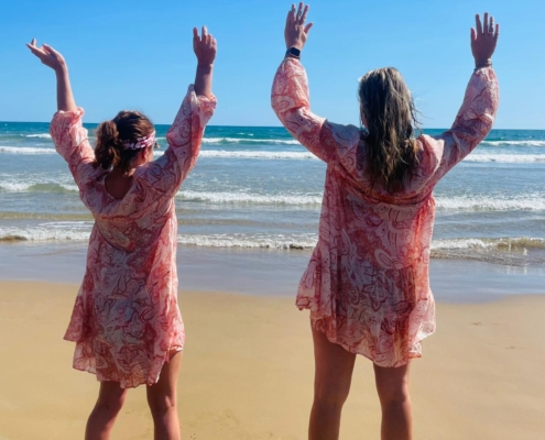 Zwei Personen stehen am Strand und schauen aufs Meer. Sie stehen mit dem Rücken zur Kamera.