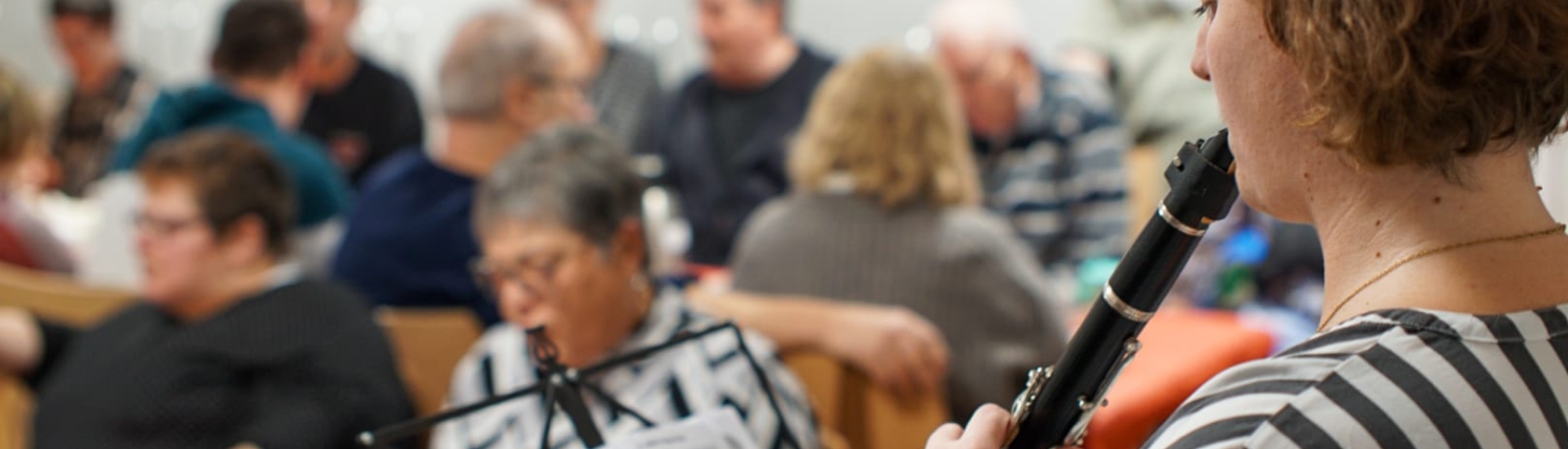 Eine Frau spielt ein Klarinetto. Sie steht vor anderen Leuten.