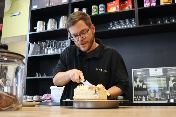 Ein Mann bäckt einen Kuchen. Er hält einen Löffel in der Hand und gibt Zutaten auf den Kuchen.