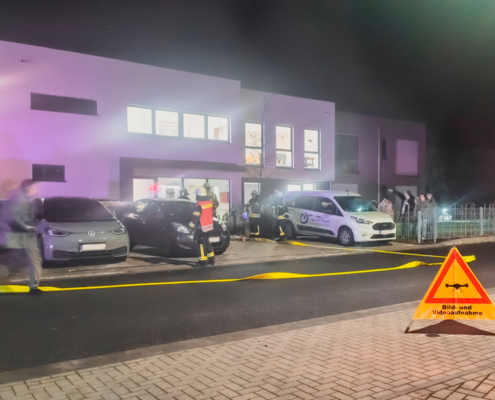 Polizei vor einem Gebäude. Es sind Autos und Menschen zu sehen. Es ist dunkel und es leuchtet Licht.