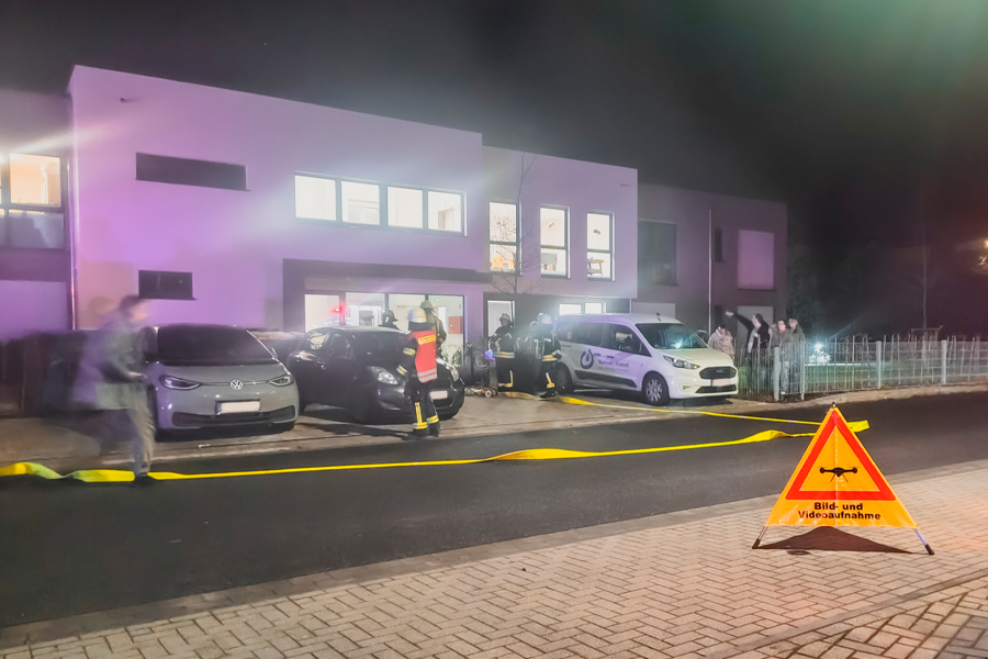 Polizei vor einem Gebäude. Es sind Autos und Menschen zu sehen. Es ist dunkel und es leuchtet Licht.