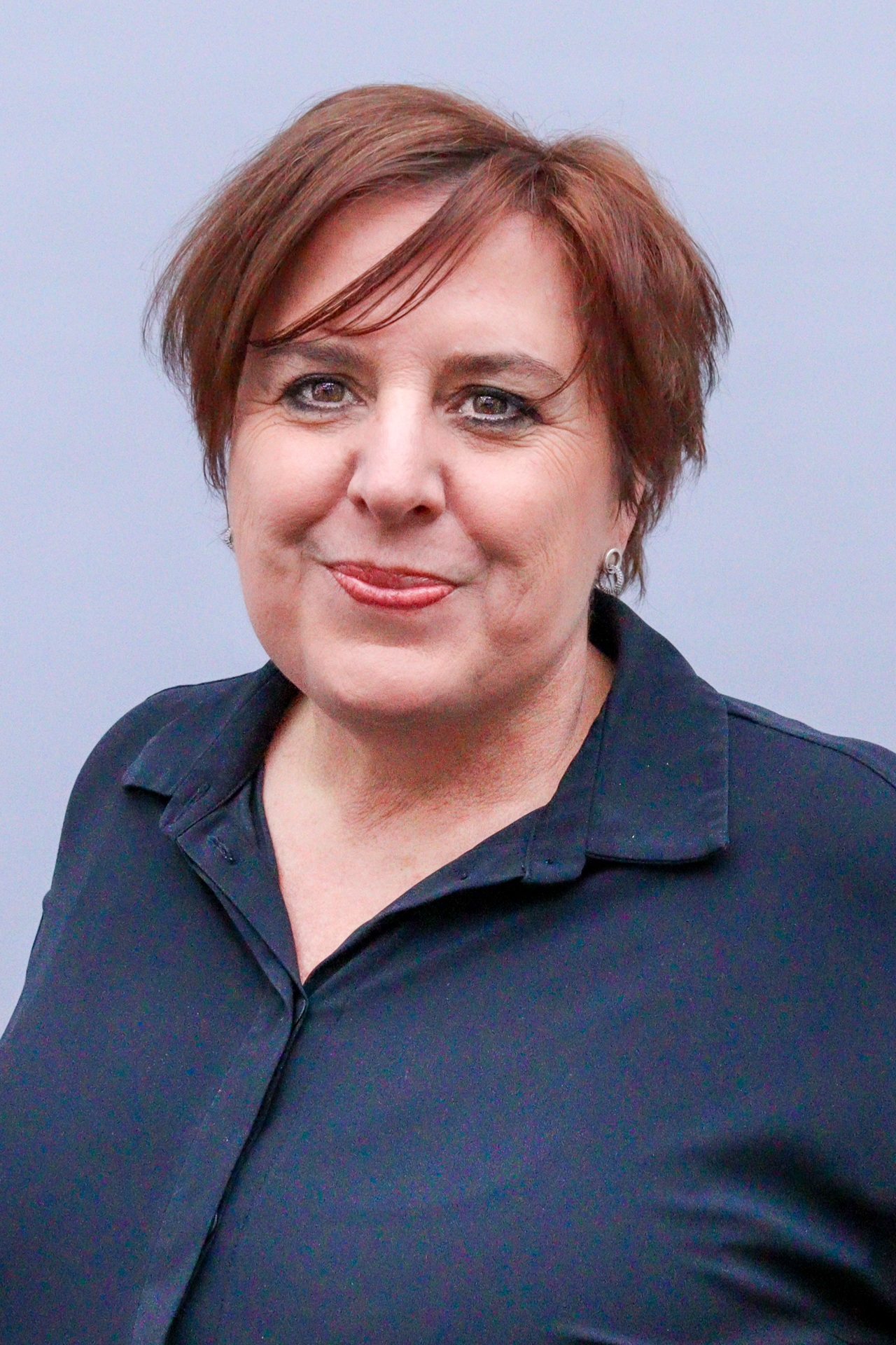 Eine Frau lächelt in die Kamera. Sie hat kurze, braune Haare und trägt ein schwarzes Hemd.