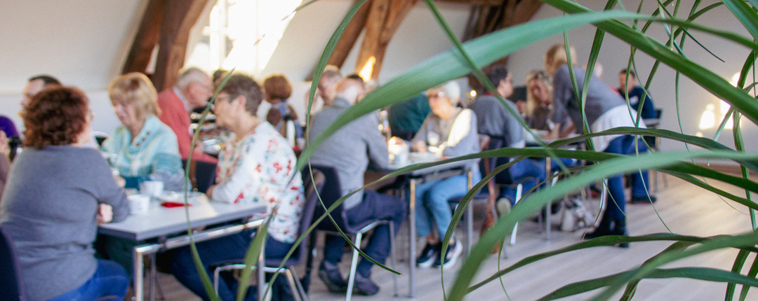 Menschen sitzen an Tischen. Sie essen und trinken. Es sieht aus wie ein Treffen oder eine Veranstaltung.