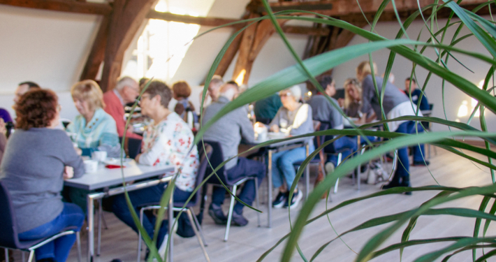 Menschen sitzen an Tischen. Sie essen und trinken. Es sieht aus wie ein Treffen oder eine Veranstaltung.