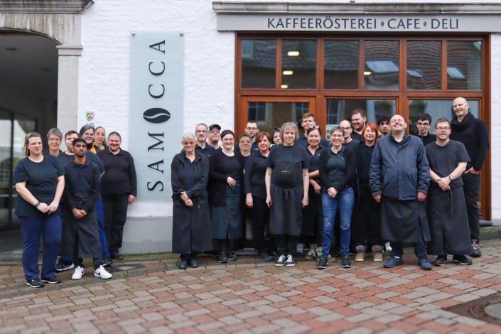 Gruppe von Mitarbeitern steht vor einer Tür. Sie tragen dunkle Arbeitskleidung.