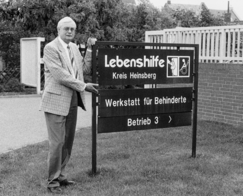 Ein Mann steht vor einem Schild. Er trägt einen Anzug. Das Schild zeigt den Namen "Kreis Heinsberg".