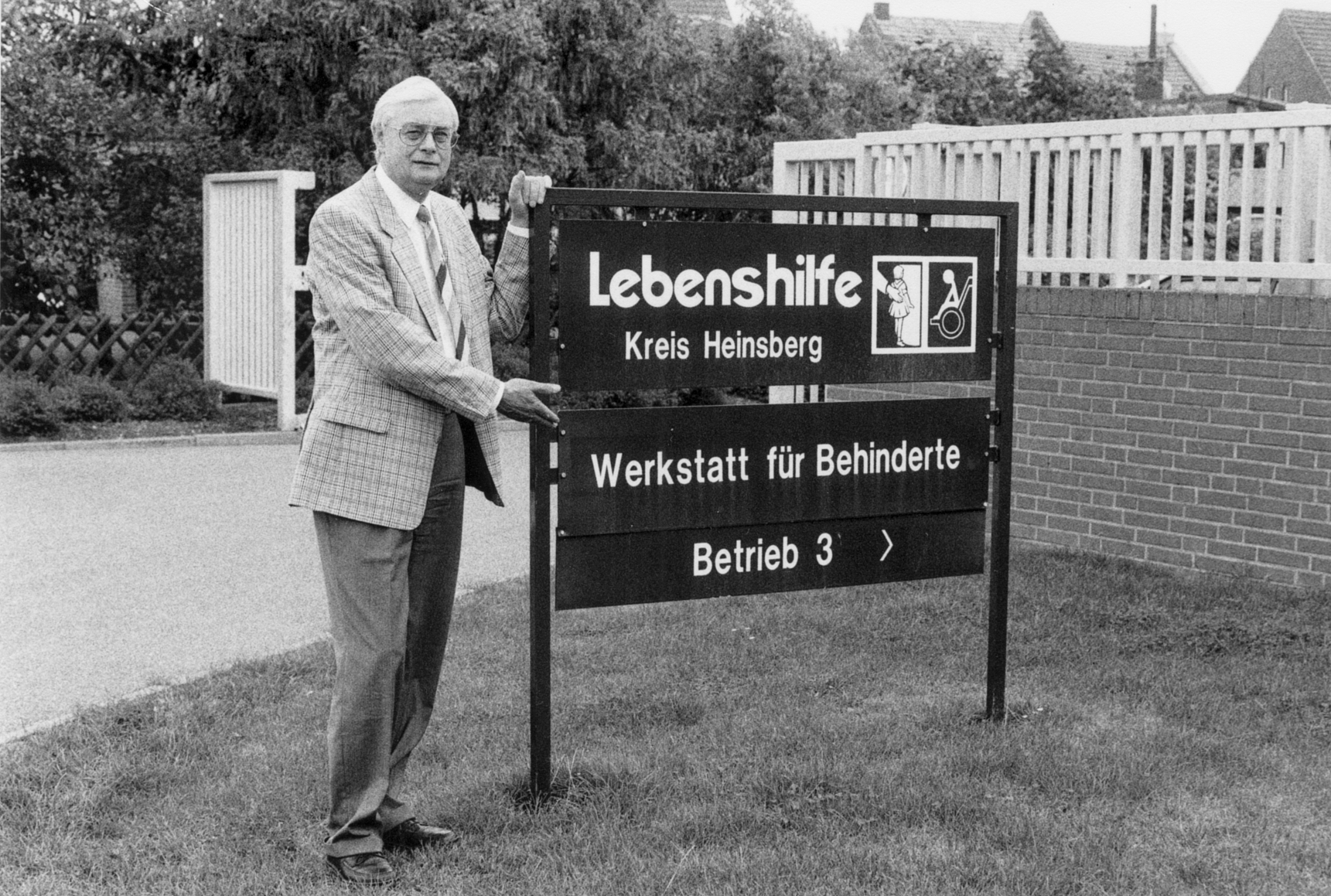 Ein Mann steht vor einem Schild. Er trägt einen Anzug. Das Schild zeigt den Namen "Kreis Heinsberg".