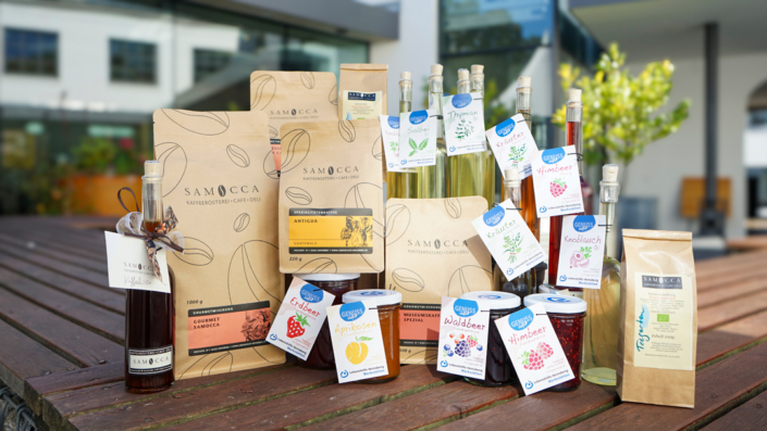 Vielerlei Marmelade und Gelee in Gläsern und ein Päckchen stehen auf einem Holztisch.