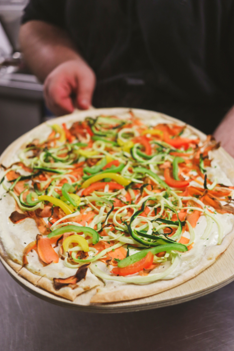 Pizza mit Tomaten und Gurken auf einem Tablett.