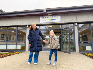 Eine Frau und ein Kind gehen zusammen. Sie halten Händchen. Sie stehen vor einem Gebäude.