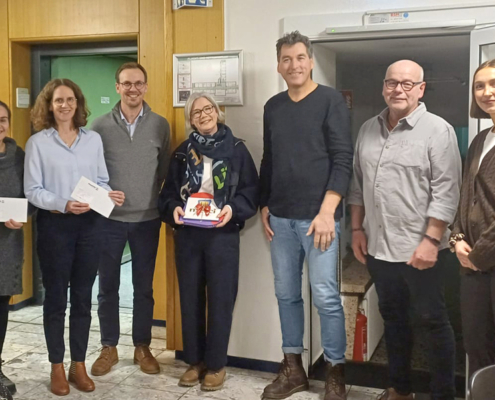 Fünf Personen stehen drinnen. Zwei Frauen und drei Männer. Sie halten Papiere in der Hand.