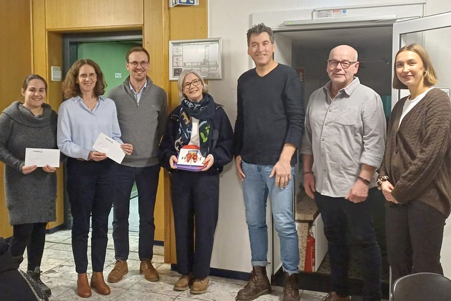 Fünf Personen stehen drinnen. Zwei Frauen und drei Männer. Sie halten Papiere in der Hand.