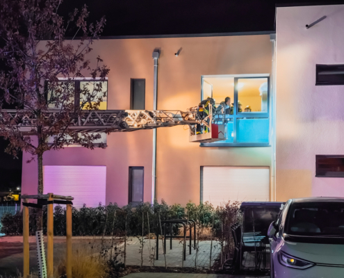 Haus mit Lichtern. Ein Auto steht vor dem Haus. Es ist dunkel draußen.