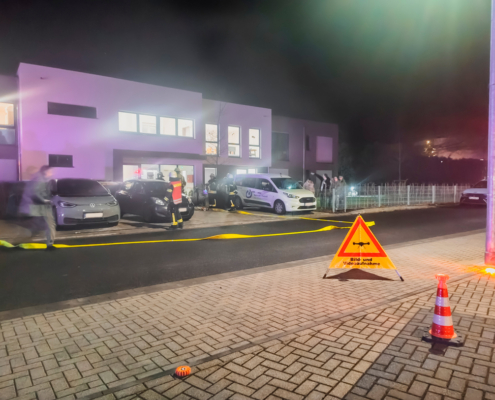 Viele Autos stehen vor einem Gebäude. Es ist dunkel und es leuchten Lichter.
