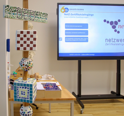 Bunte Bauklötze stehen auf einer Holzbank. Ein Bildschirm steht daneben.