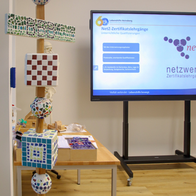 Bunte Bauklötze stehen auf einer Holzbank. Ein Bildschirm steht daneben.